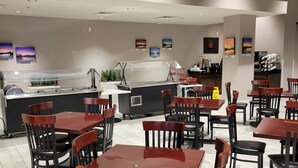 Un restaurante con varias mesas y sillas, una barra con vitrina y obras de arte en las paredes.