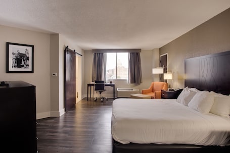 A hotel room with a large bed, a desk, a chair, and a window with curtains.