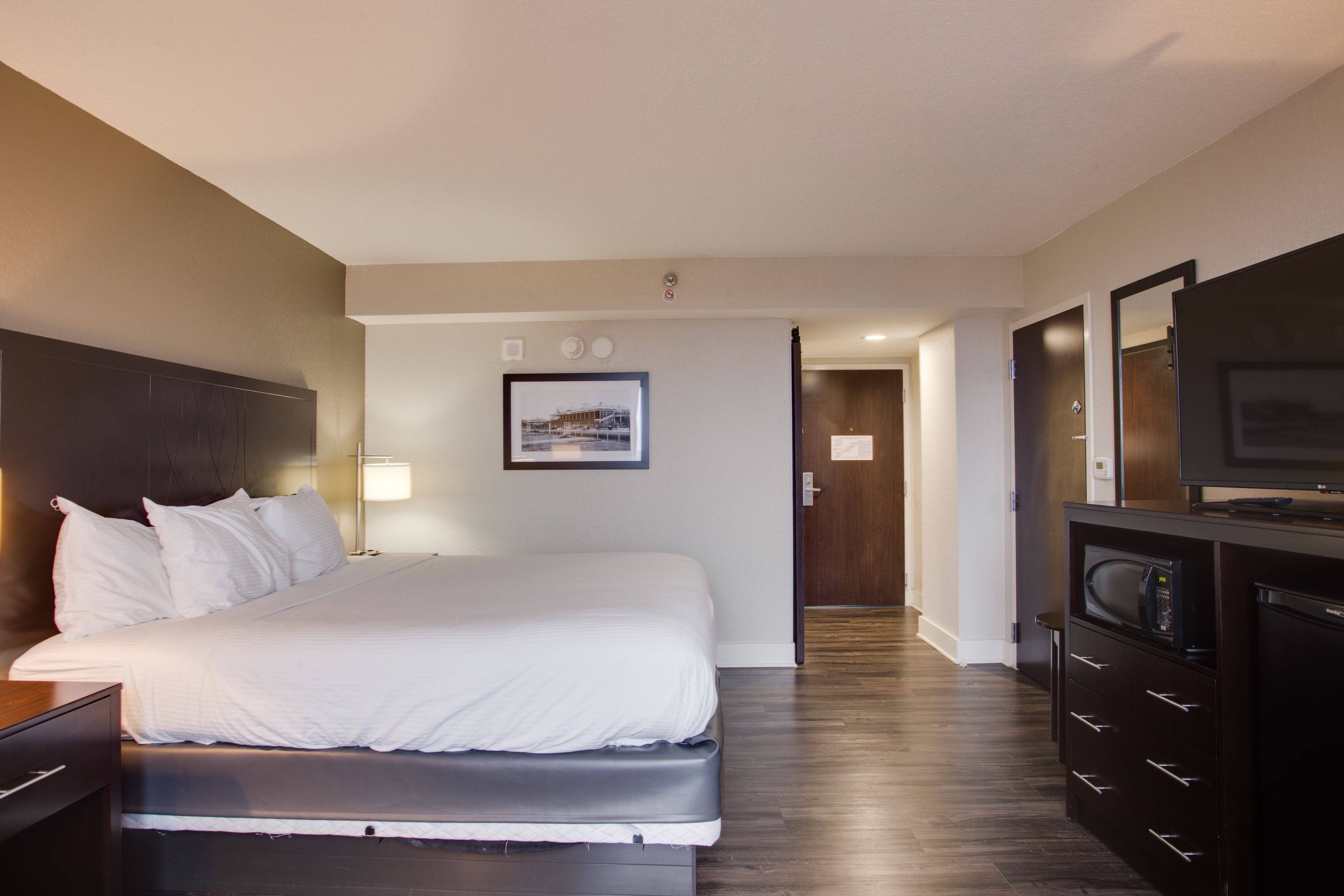 Quarto de hotel com uma cama, televisão, escrivaninha e espelho.