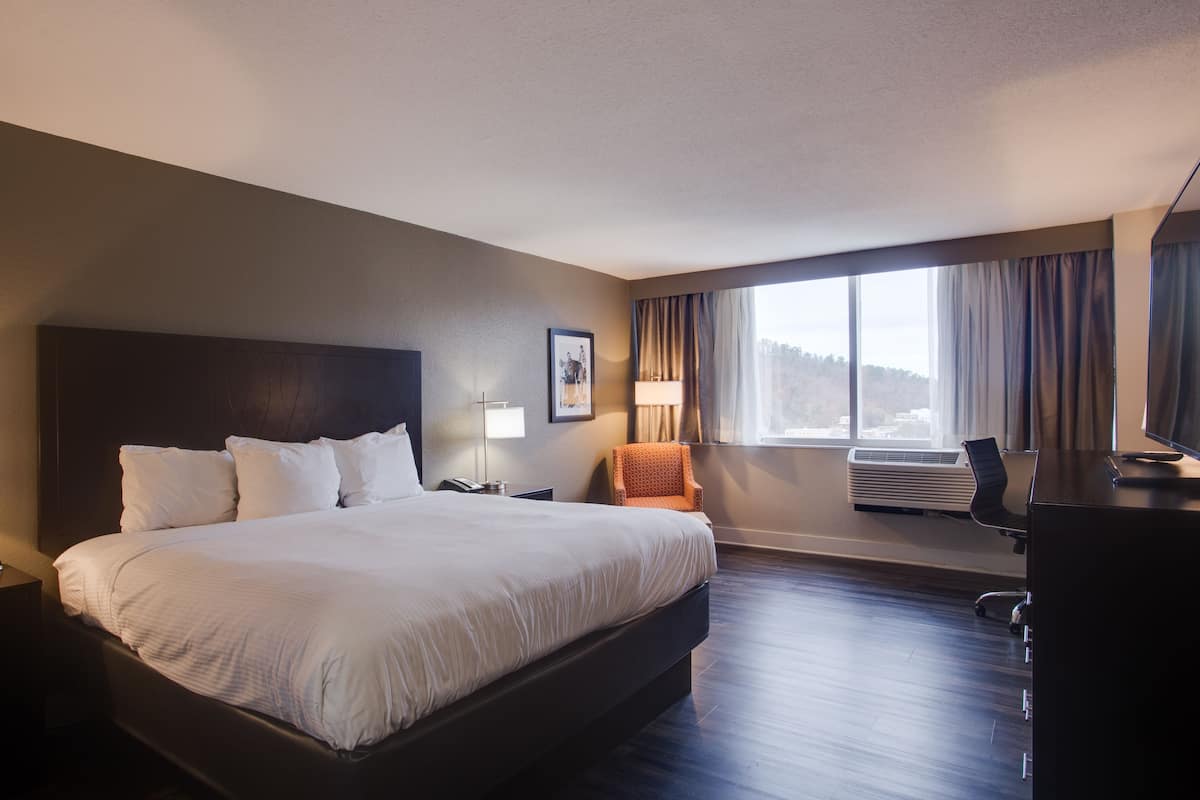 Habitación de hotel con una cama grande, un escritorio, una silla, una l ámpara y una ventana con cortinas.