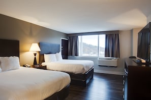A hotel room with two beds, a desk, a TV, and a window with curtains.