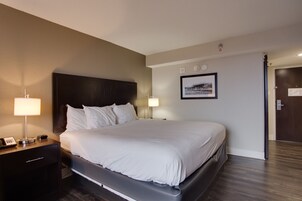 Habitación de hotel con una cama grande, lámparas de noche, una mesita y un cuadro en la pared.
