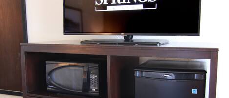 Ett litet, praktiskt kök med mikrovågsugn, ett litet kylskåp och en platt-TV som är monterad på ett träskåp.