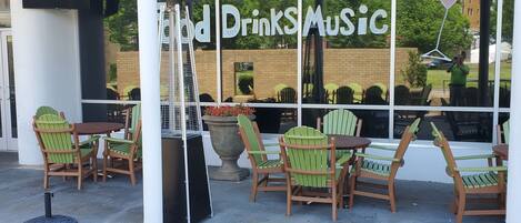 An outdoor seating area with green chairs and tables, a large planter, and a sign for 'BAR N' GRILL Food & Drink Music'.