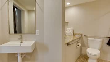 Une salle de bain avec un lavabo blanc, un miroir, des toilettes et une barre d’appui.