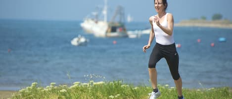 A person jogging on a grassy area near a body of water with boats in the background.