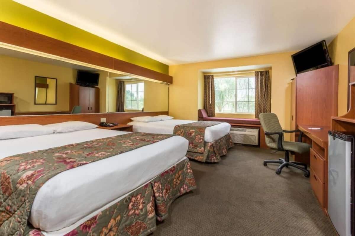 A hotel room with two beds, a desk, a chair, a television, and a window with curtains.