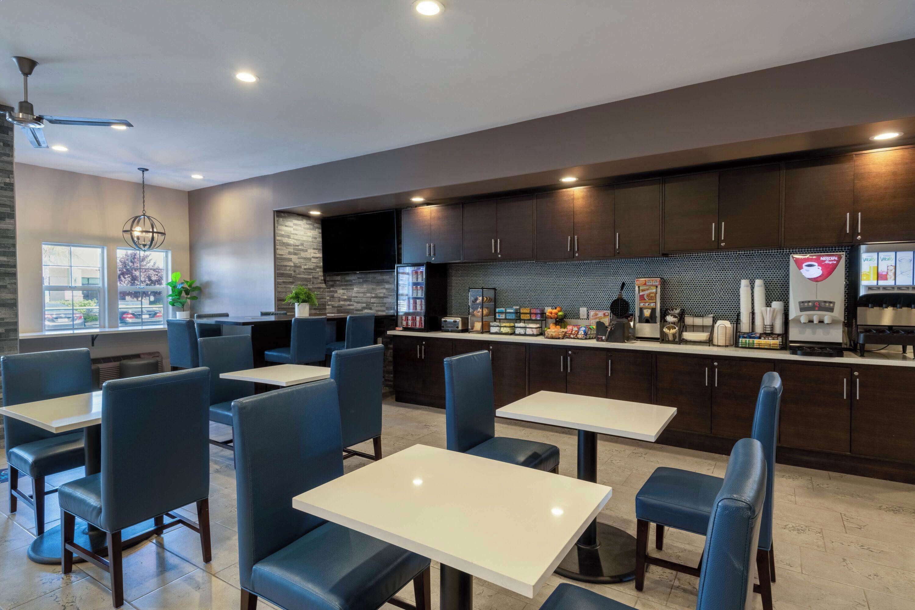 A modern restaurant with dark wooden cabinets, white tables, and blue chairs.