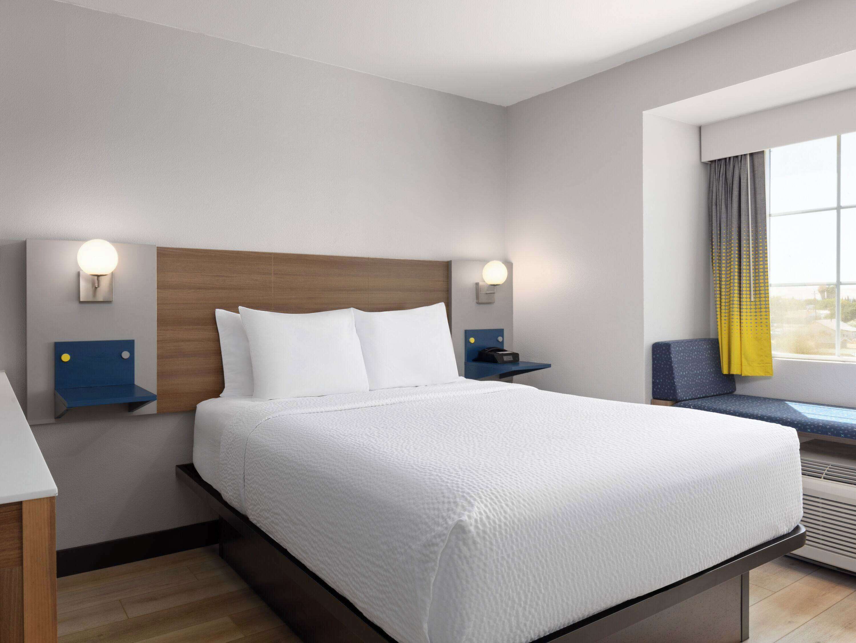 Habitación de hotel con una cama grande, mesitas de noche, una ventana con cortinas y vistas al exterior.