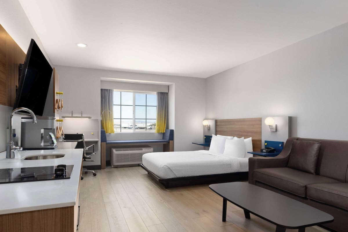 A modern hotel room with a kitchenette, a bed, a sofa, and a small table.
