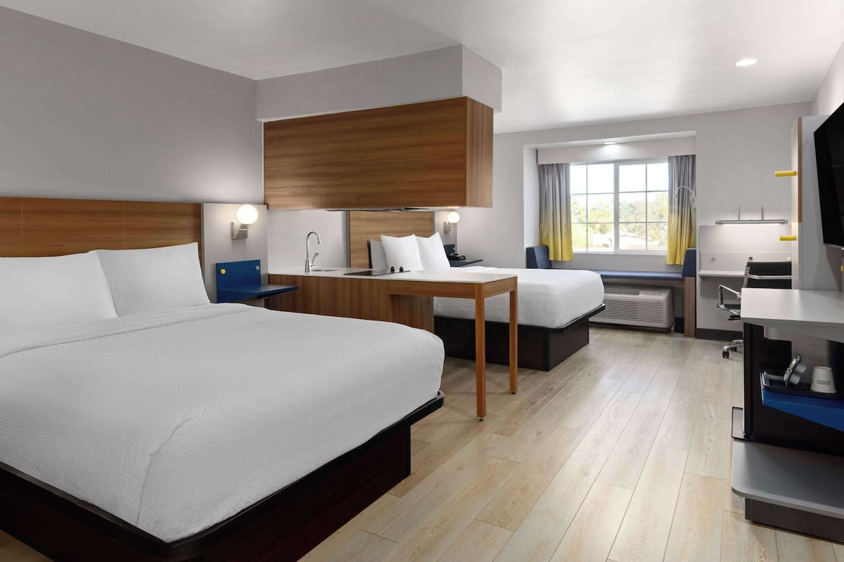 A hotel room with a large bed, a desk with a chair, a small table, a sofa, a TV, and a window with curtains.