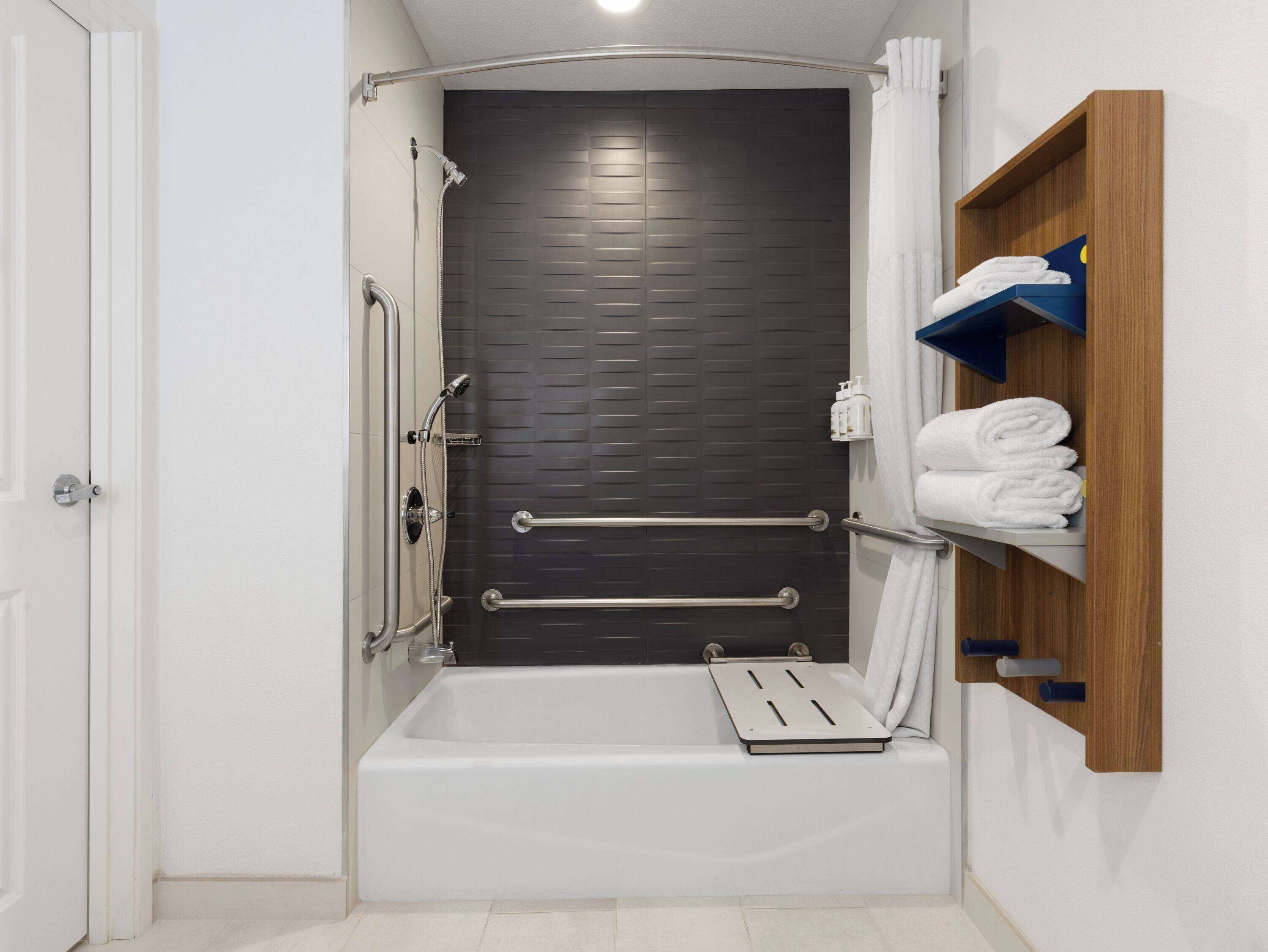 Une salle de bain moderne équipée d’une baignoire, de barres d’appui, d’un pommeau de douche et d’un porte-serviettes.