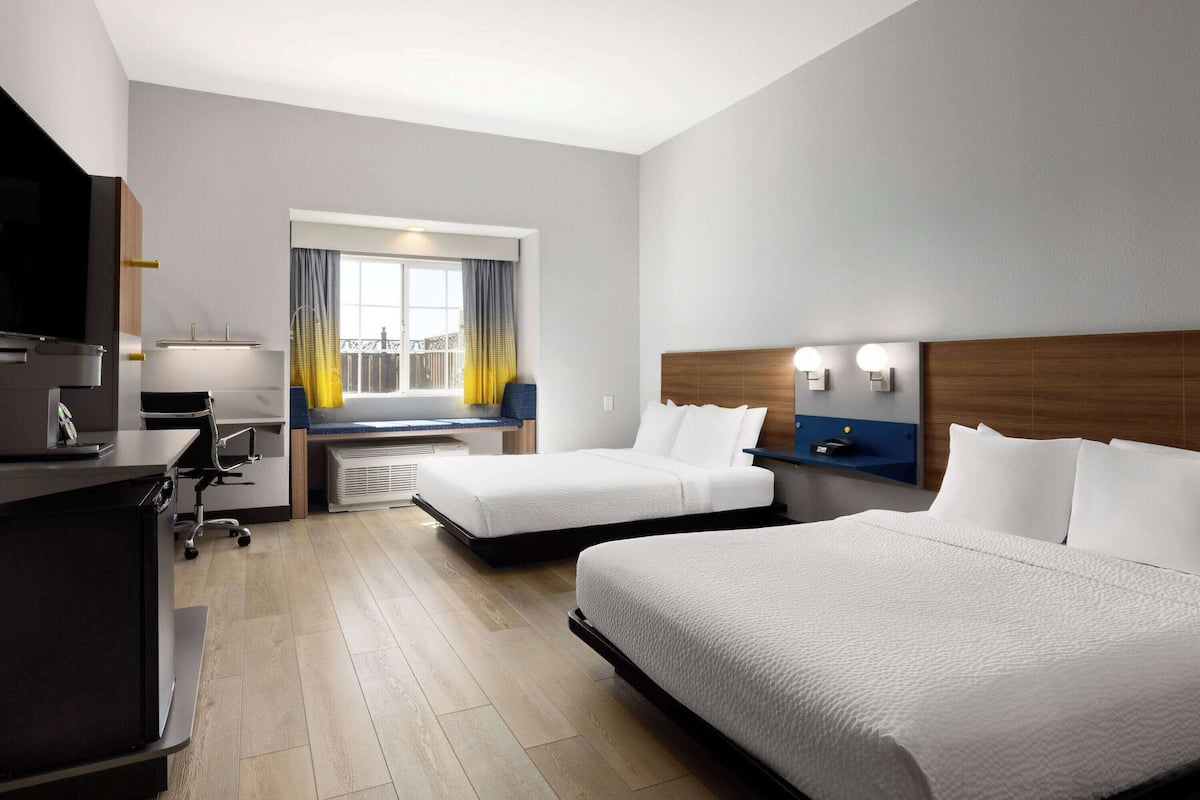 A modern hotel room with two beds, a desk with a chair, a television, and a window with curtains.