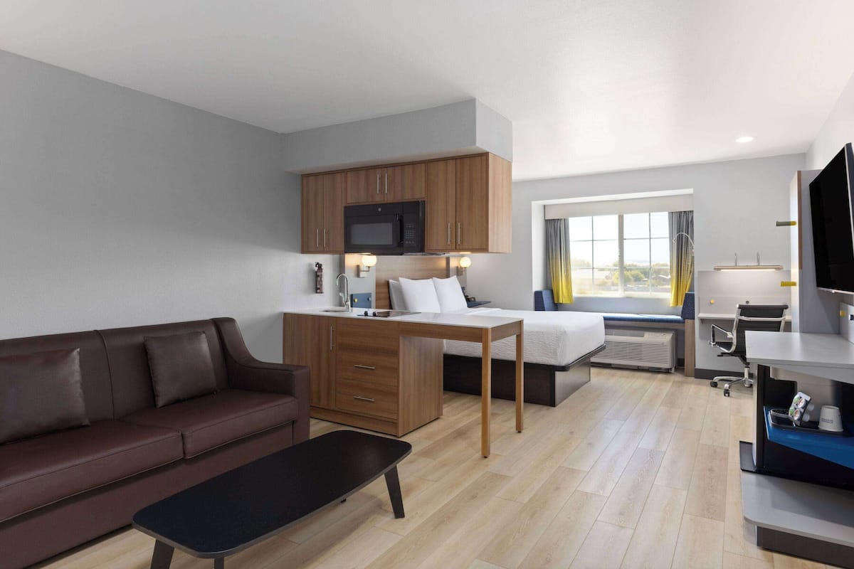 A compact hotel room with a kitchenette, a sofa, a bed, and a desk.