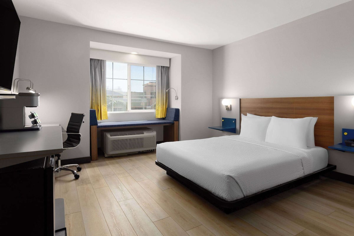 A hotel room with a bed, desk, chair, and a window with curtains.
