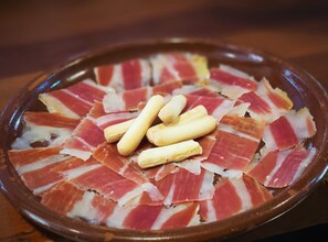 A plate of sliced cured meat with whole garlic cloves on a ceramic dish.