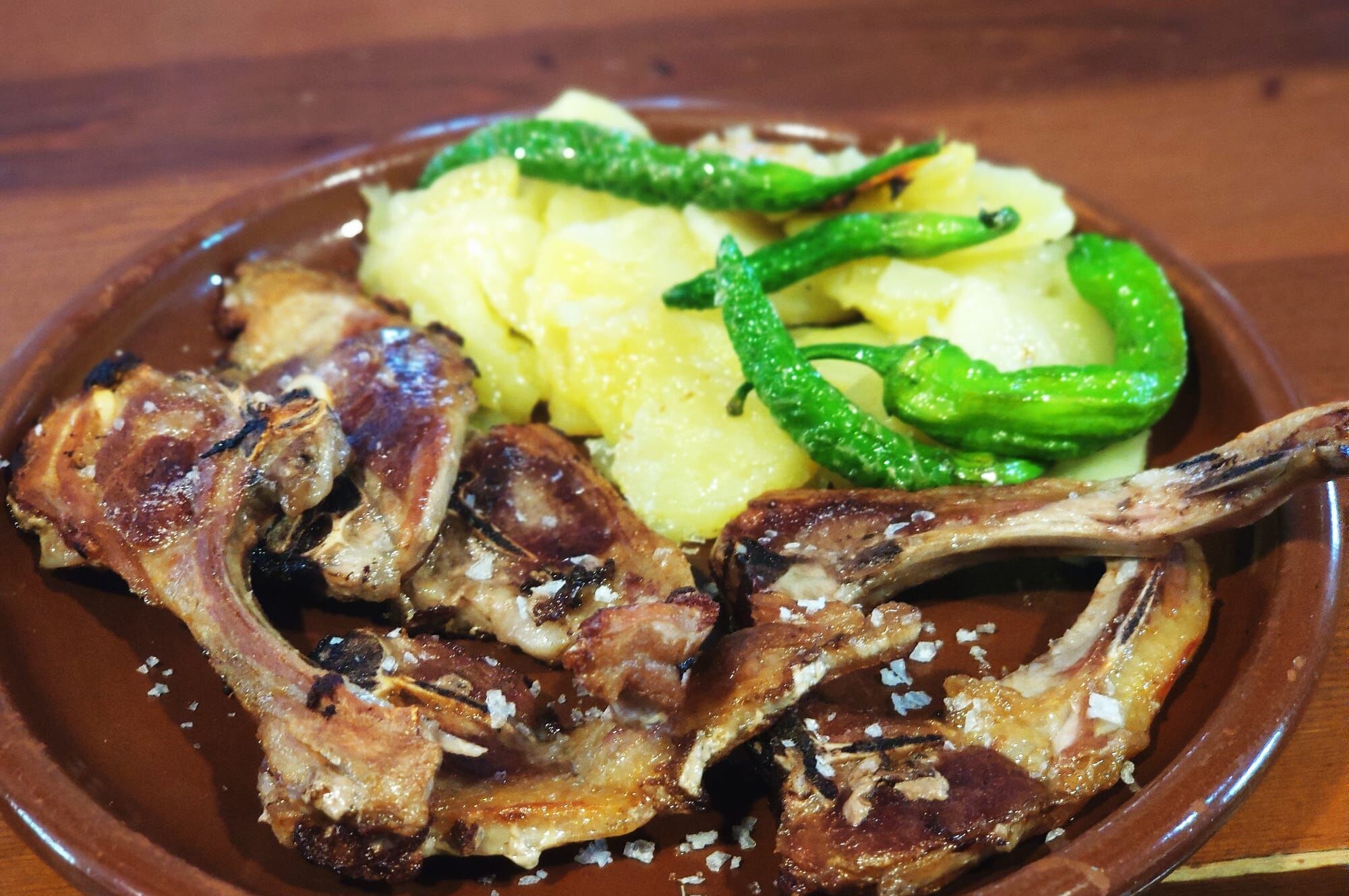 A plate with grilled lamb chops, boiled potatoes, and green peppers.