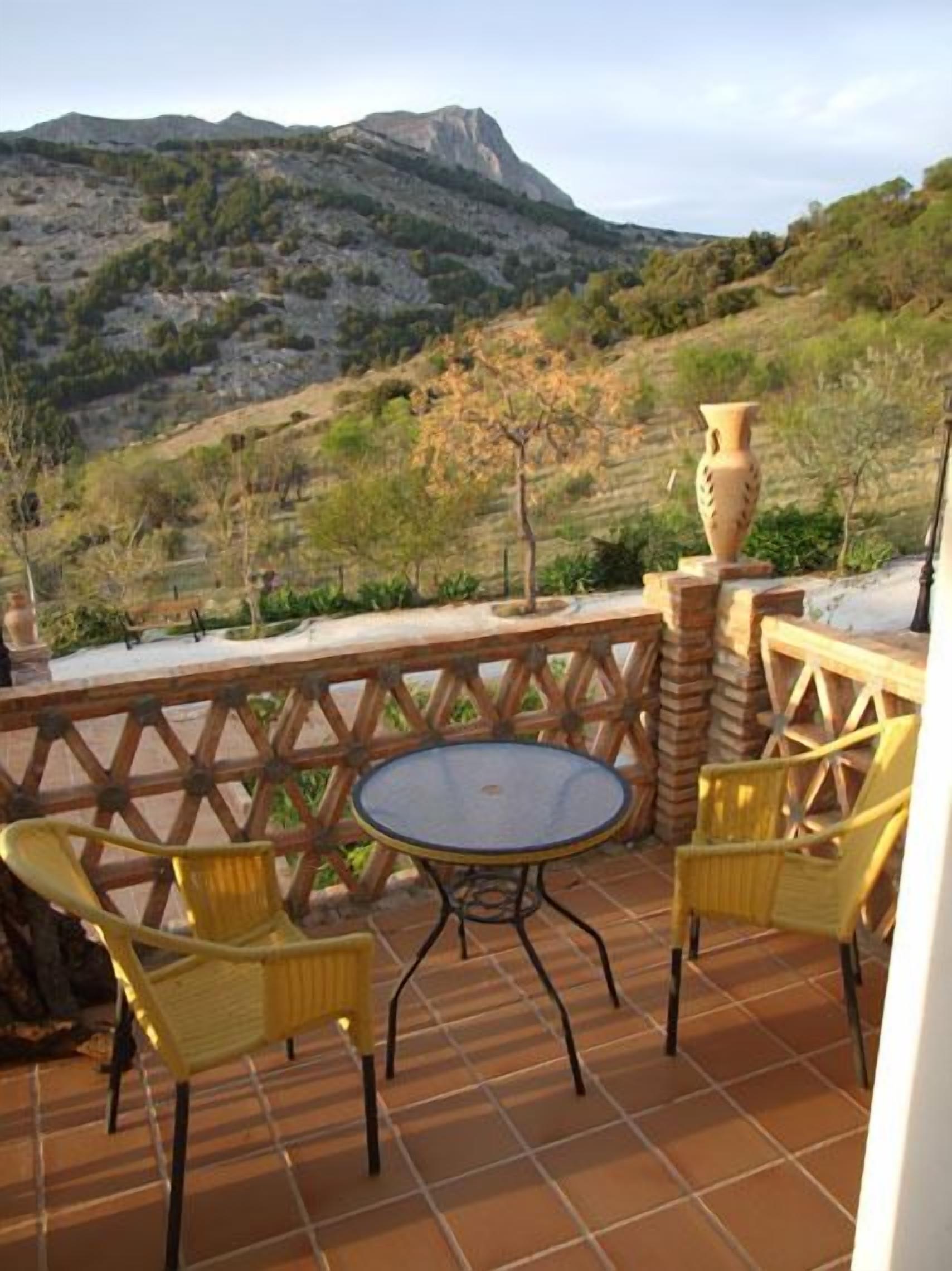 A terrace with a round table and two chairs, overlooking a mountainous landscape.