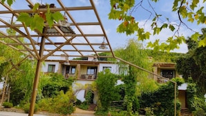 En innergård med en pergola, en vit byggnad med balkonger och frodig grönska.