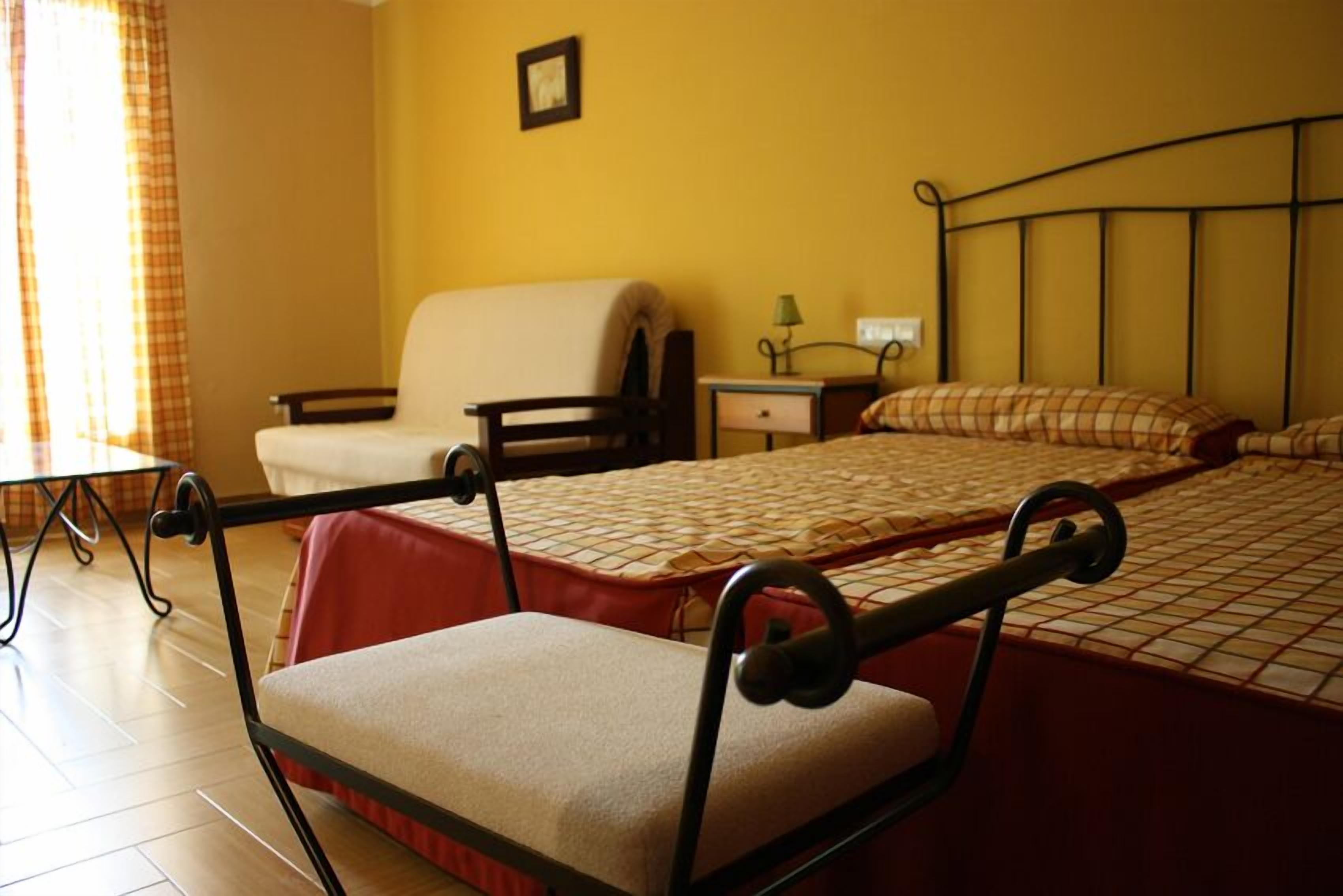 Una habitación de hotel con cama, una silla, una mesita y una mesita de noche.