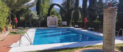 A rectangular swimming pool with a tiled edge, surrounded by a brick border and a grassy area.