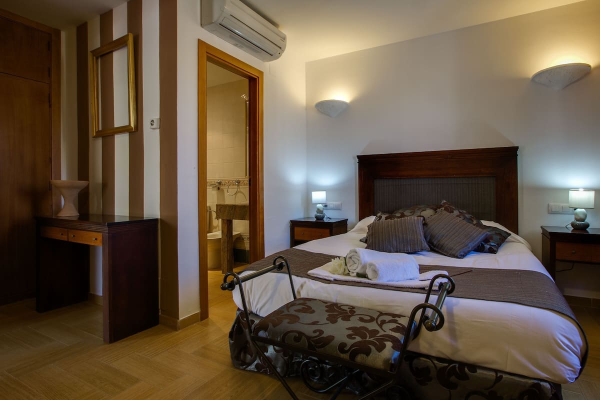 Una habitación de hotel con cama, mesitas de noche, escritorio y aire acondicionado.