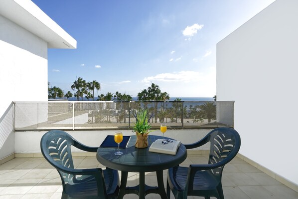 A balcony with a round table, two chairs, a potted plant, and two glasses of orange juice.
