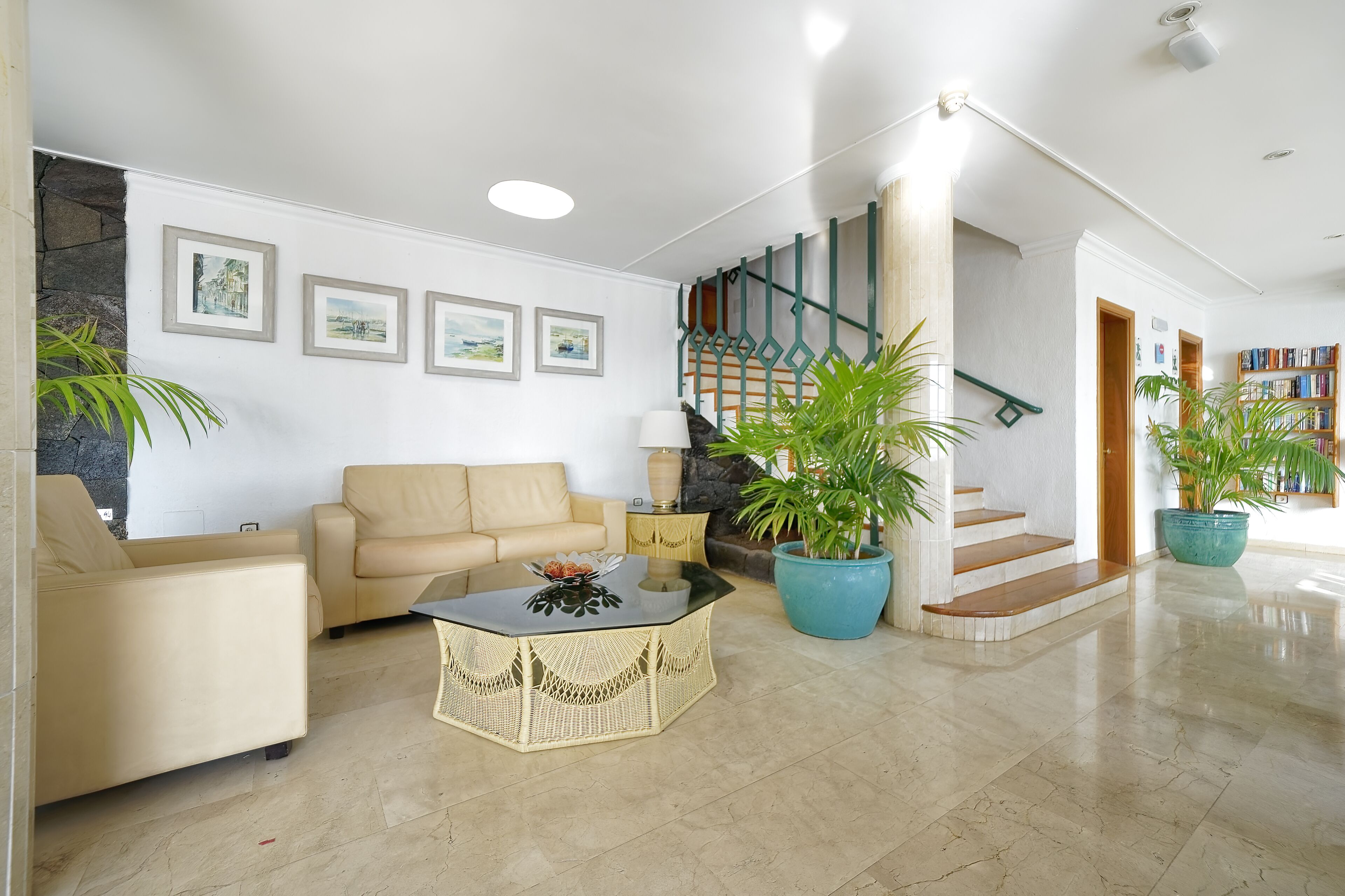 Amplia sala de estar con un sofá color beige, una mesa de centro de vidrio y una escalera con barandilla verde.