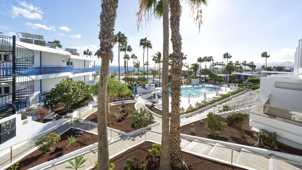 Ett semesterhotell med poolområde, palmer och utsikt över havet.