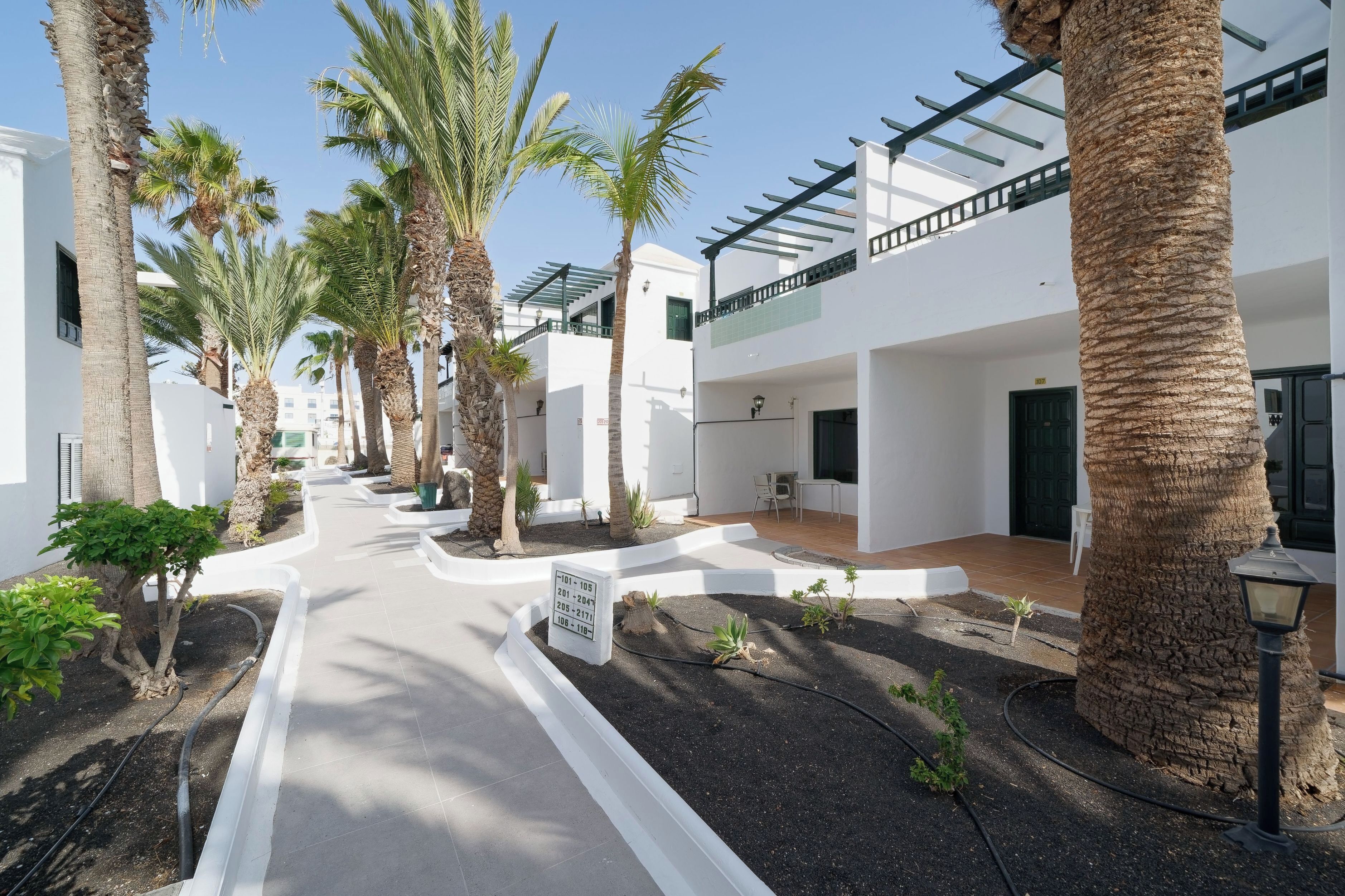 A courtyard with palm trees, white buildings, and a sign indicating room numbers.