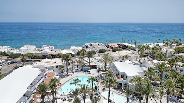 Een resort met een groot zwembad, omgeven door palmbomen en uitzicht op zee.
