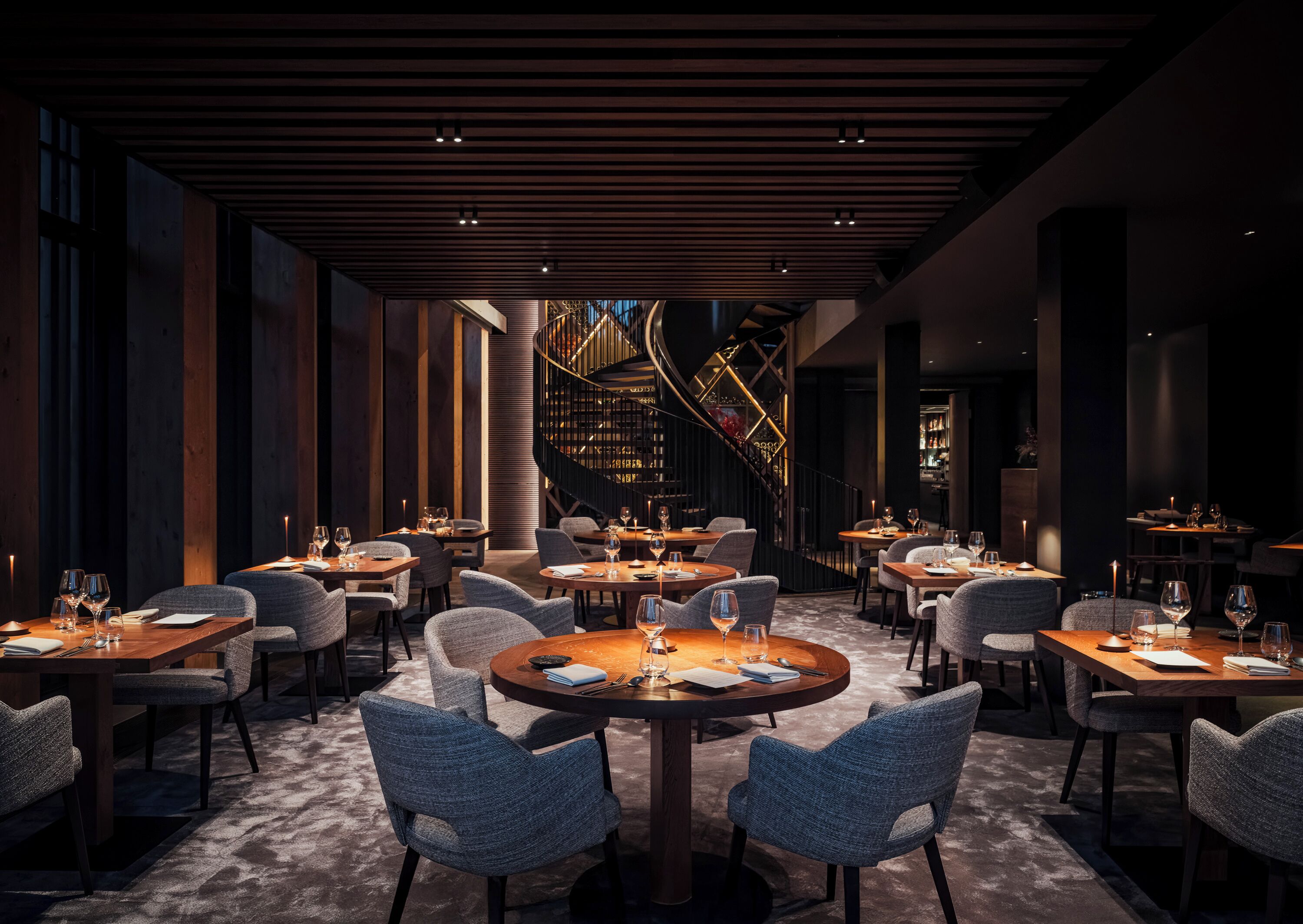 A modern restaurant with round tables and grey upholstered chairs.