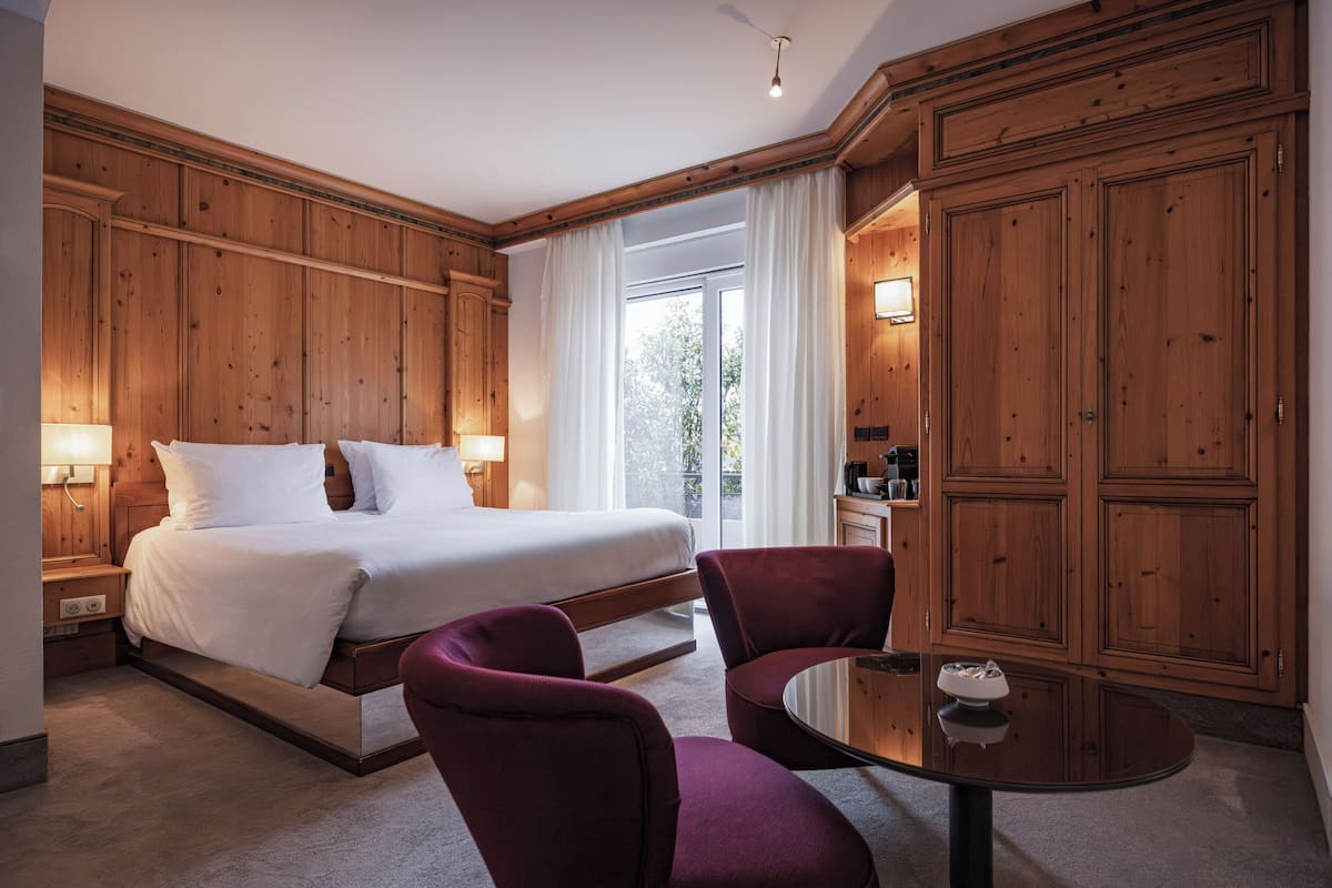Une chambre d’hôtel avec un lit, deux chaises, une table et un lambris en bois.