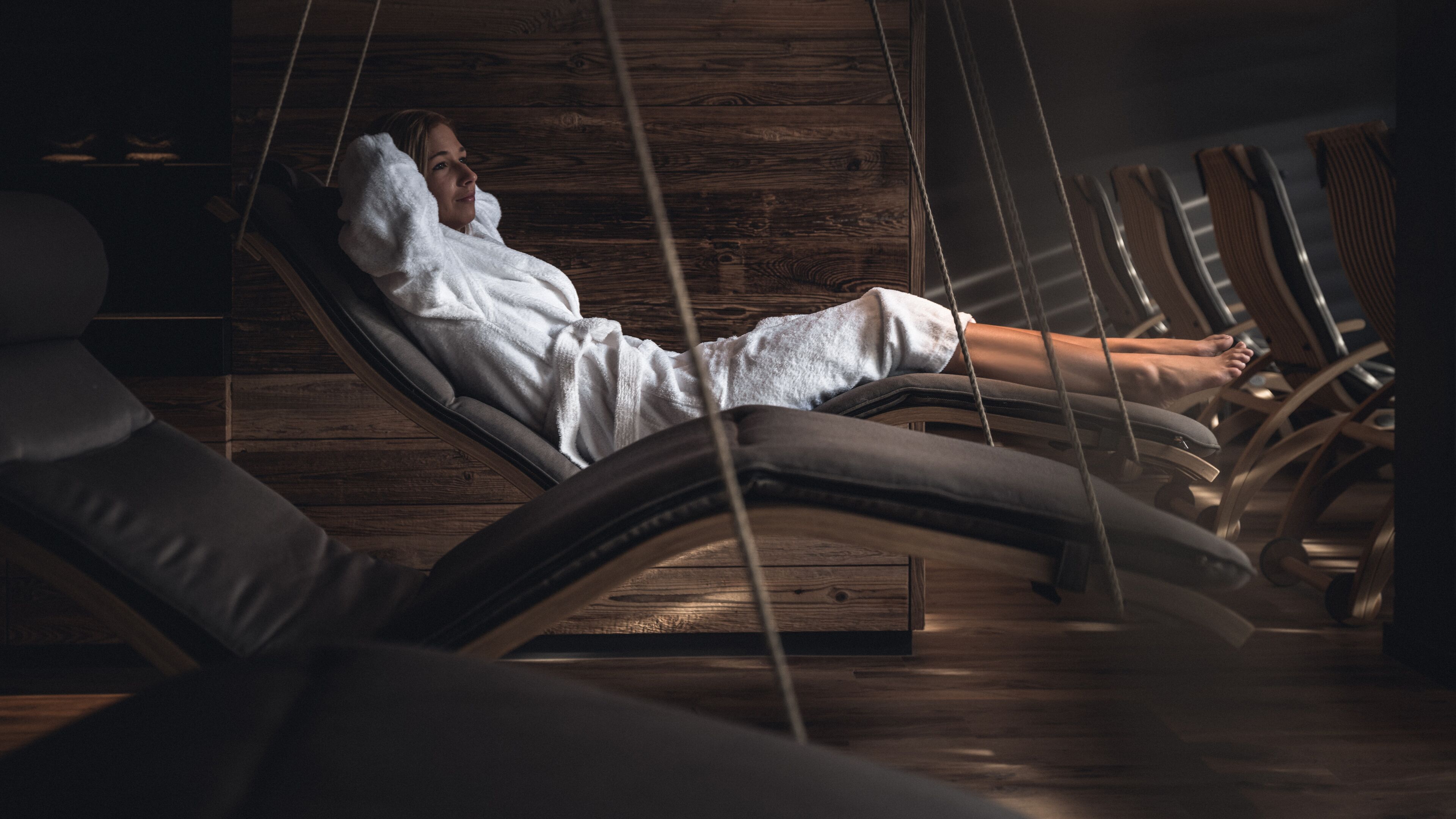 Une personne se détend dans une pièce aménagée comme un chalet en bois, avec un fauteuil de massage et un plancher en bois.