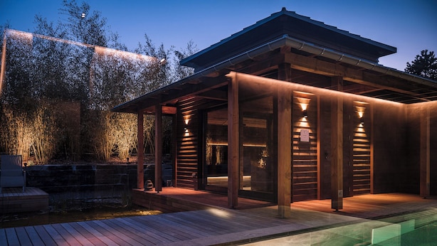 A modern outdoor pool area with wooden deck and a covered seating area.