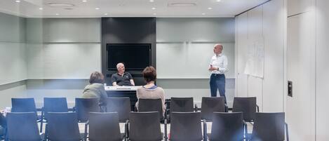 A conference room with a large screen, a presentation table, and several chairs arranged for attendees.