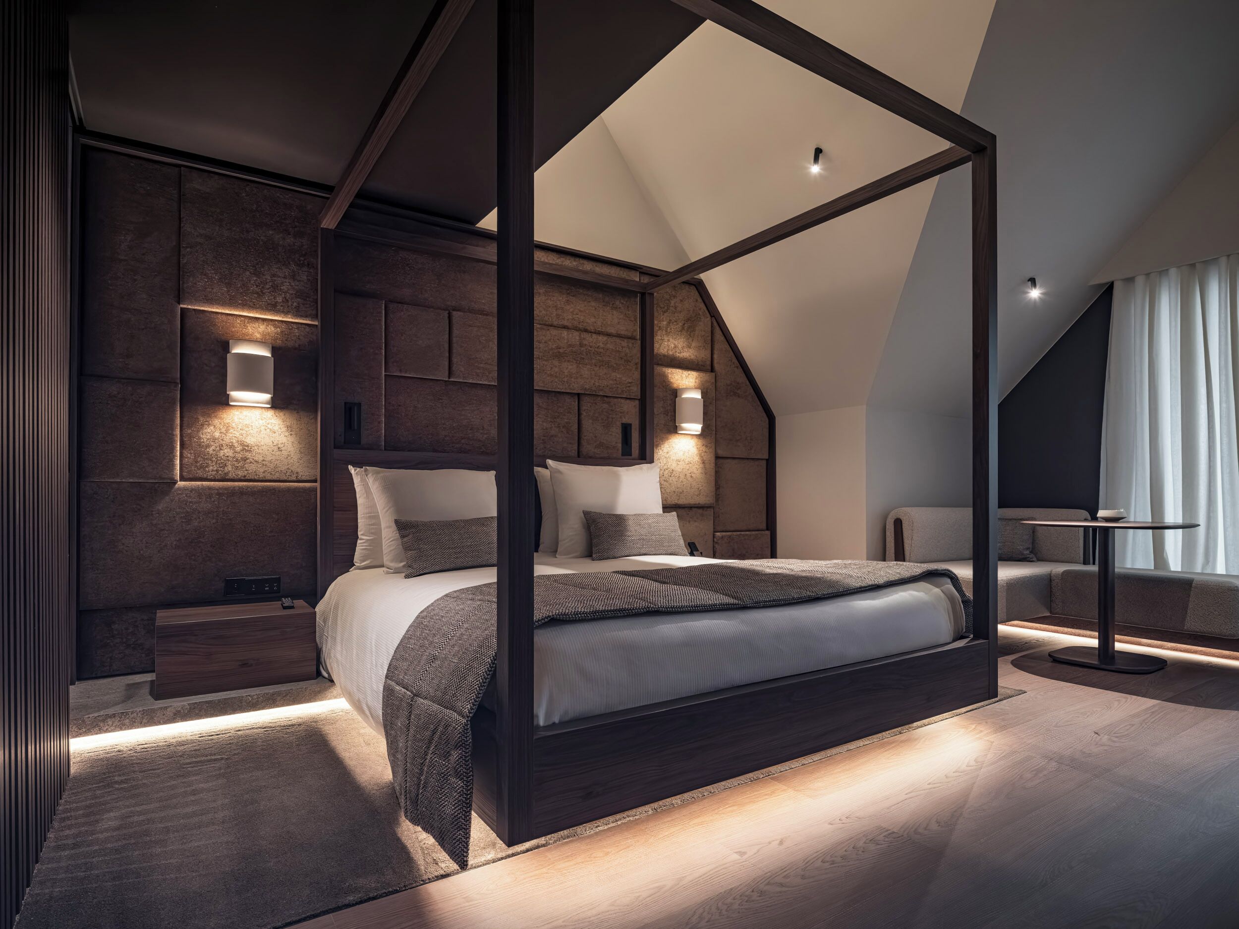 Un dormitorio moderno con cama con dosel, iluminación integrada y techo inclinado.