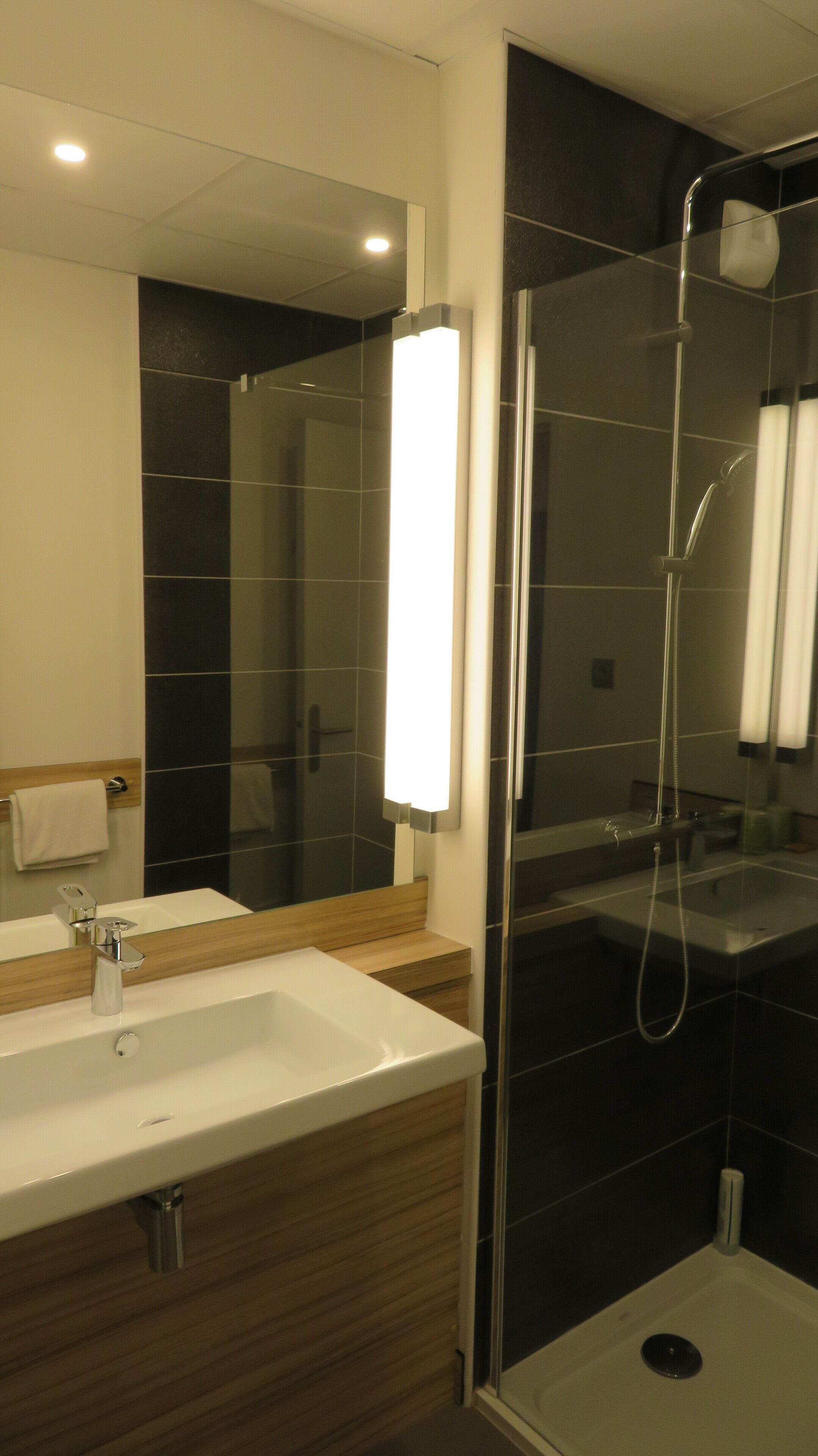 A modern bathroom with a white sink, a mirror, and a glass-enclosed shower.