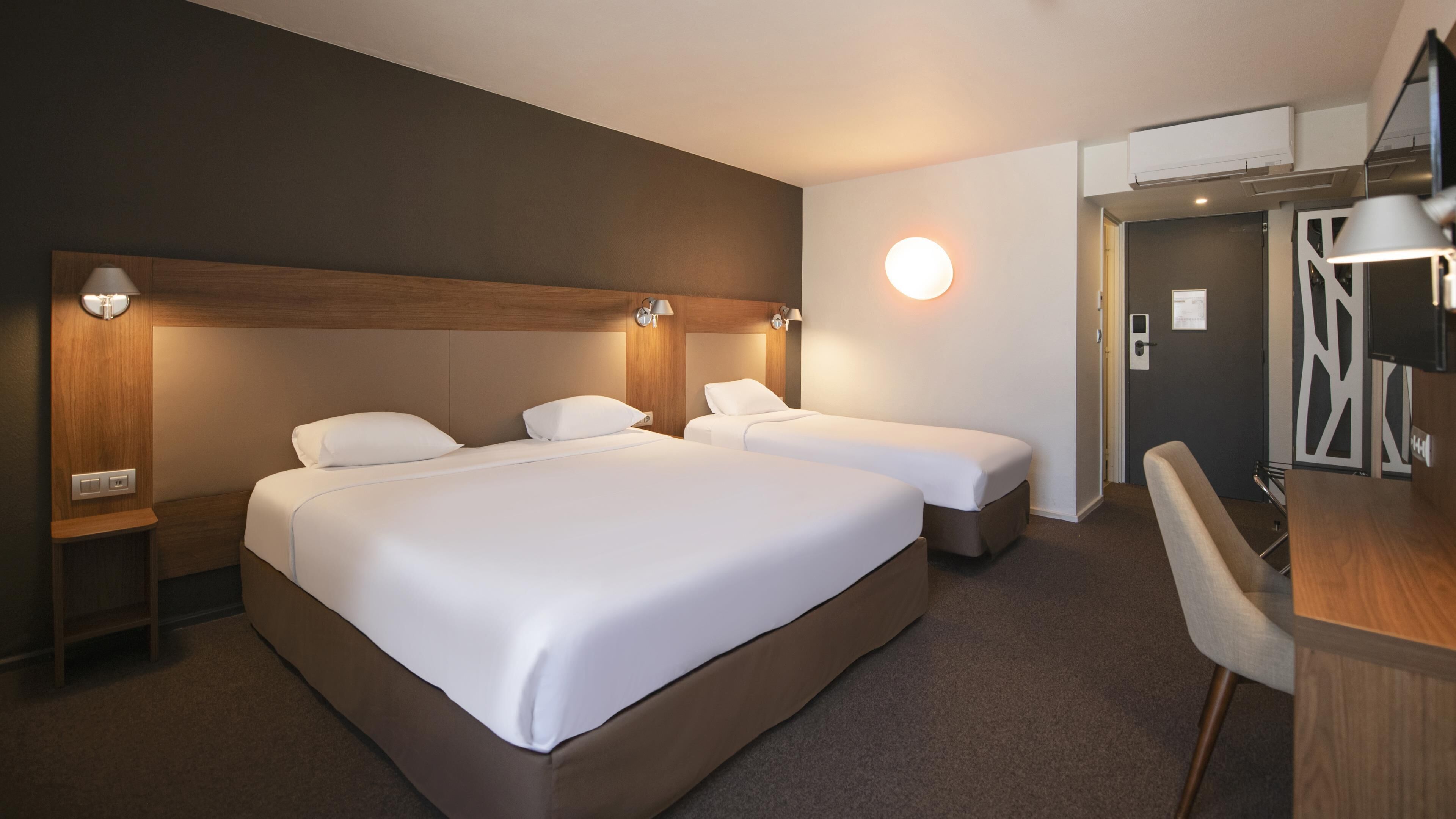 A hotel room with two beds, a desk, and a chair.