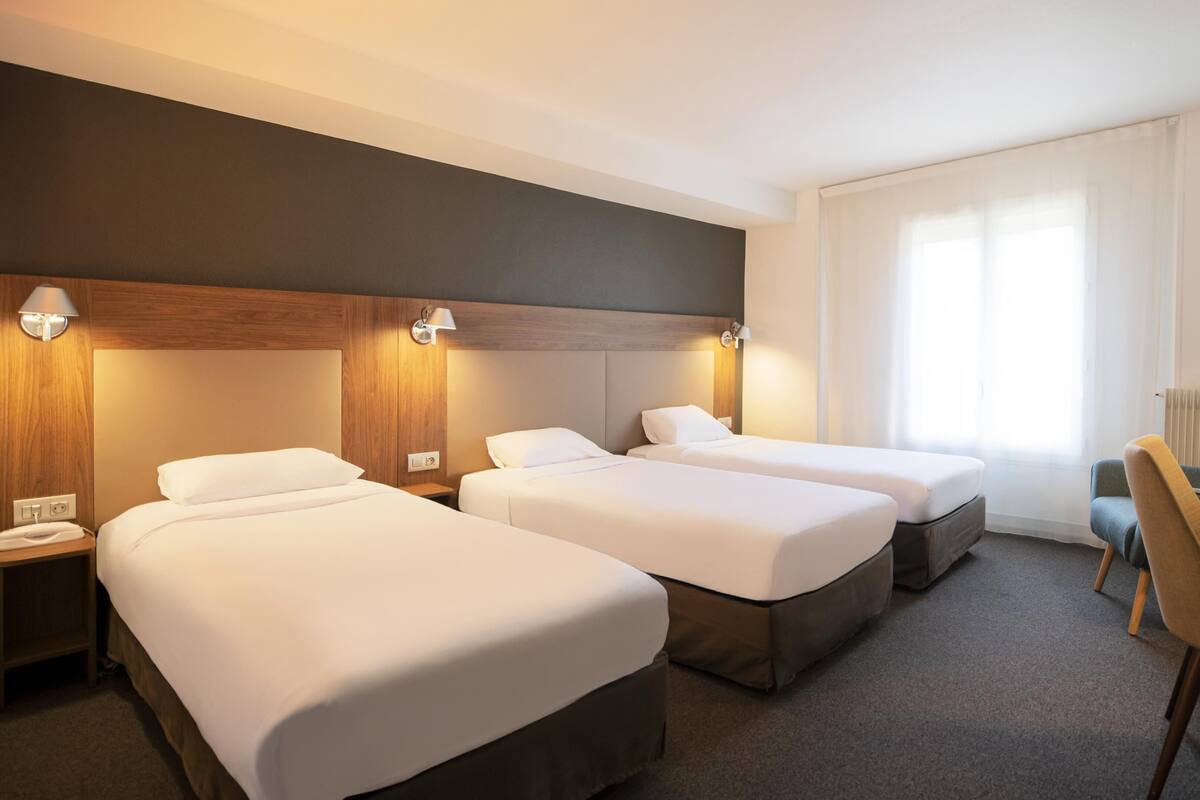 Quarto de hotel com três camas, uma escrivaninha e uma cadeira.