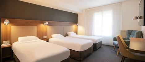 Habitación de hotel con tres camas, un escritorio y una silla.