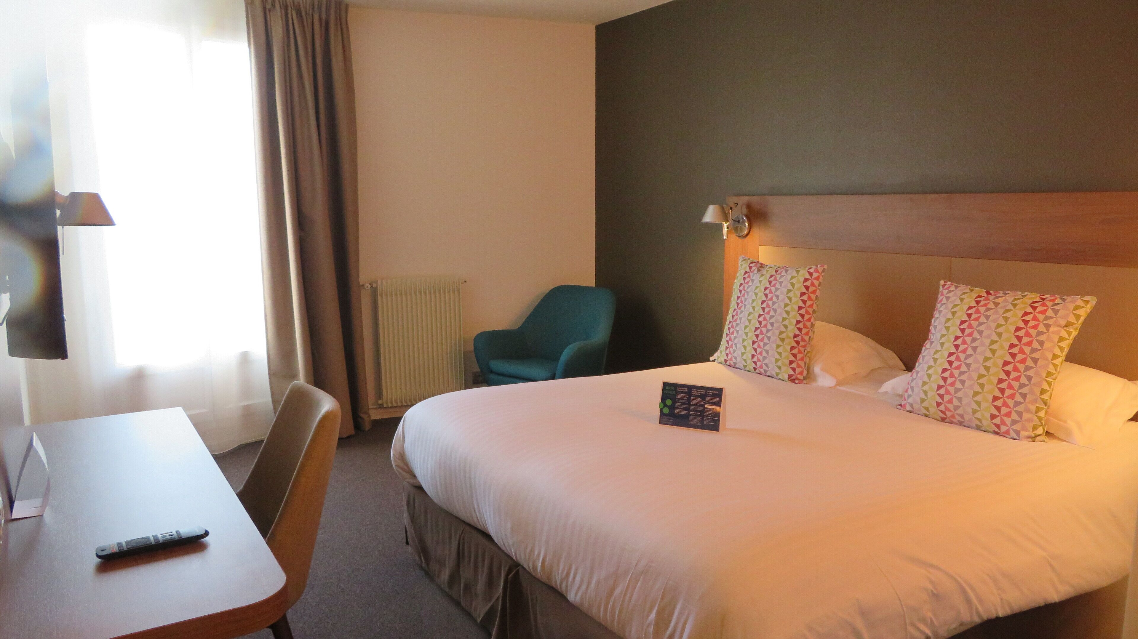 A hotel room with a bed, a desk, a chair, and a lamp.
