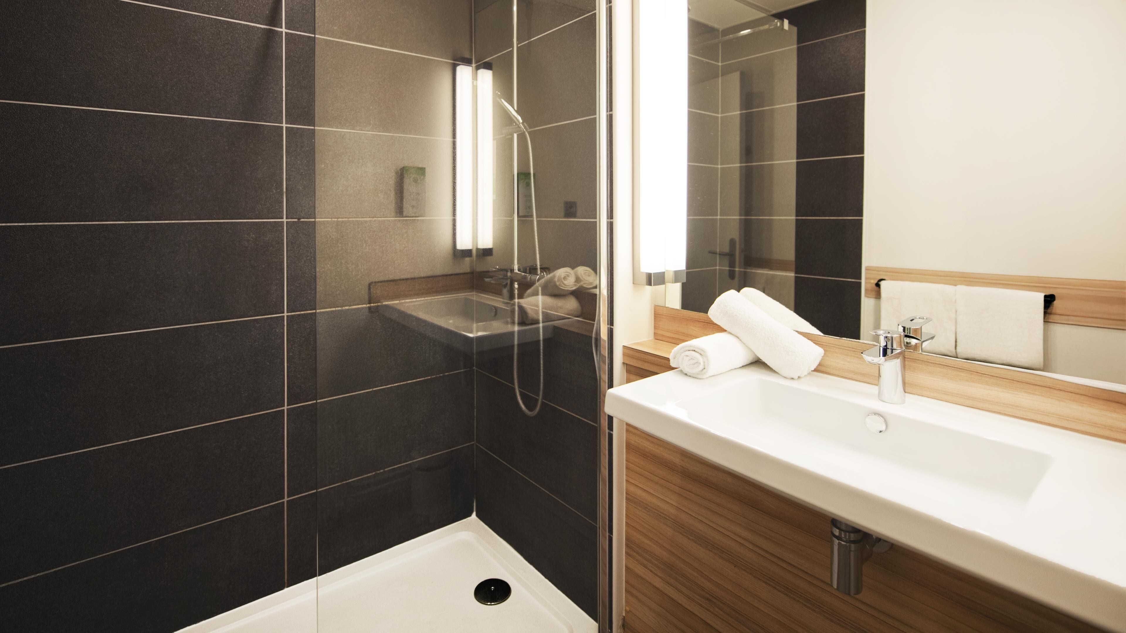 A modern bathroom with a glass-enclosed shower, a white sink, and a wooden vanity.