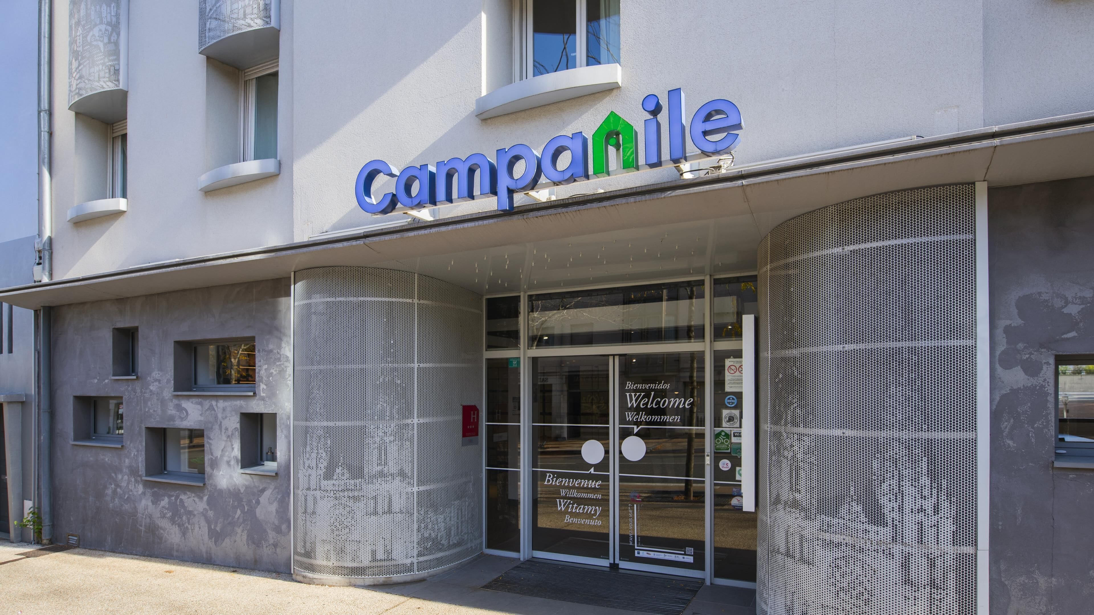 A building with a sign reading "Campanile" and a welcome sign in multiple languages.