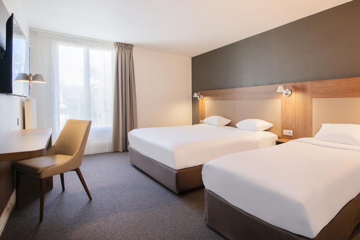 Quarto de hotel com duas camas, uma mesa e uma cadeira.