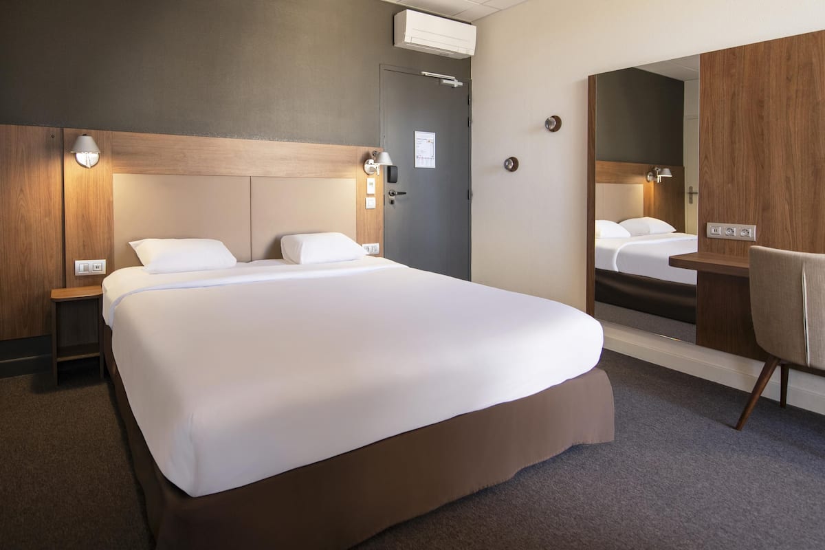 Quarto de hotel com uma cama grande, mesas de cabeceira, escrivaninha com cadeira, espelho e ar condicionado.