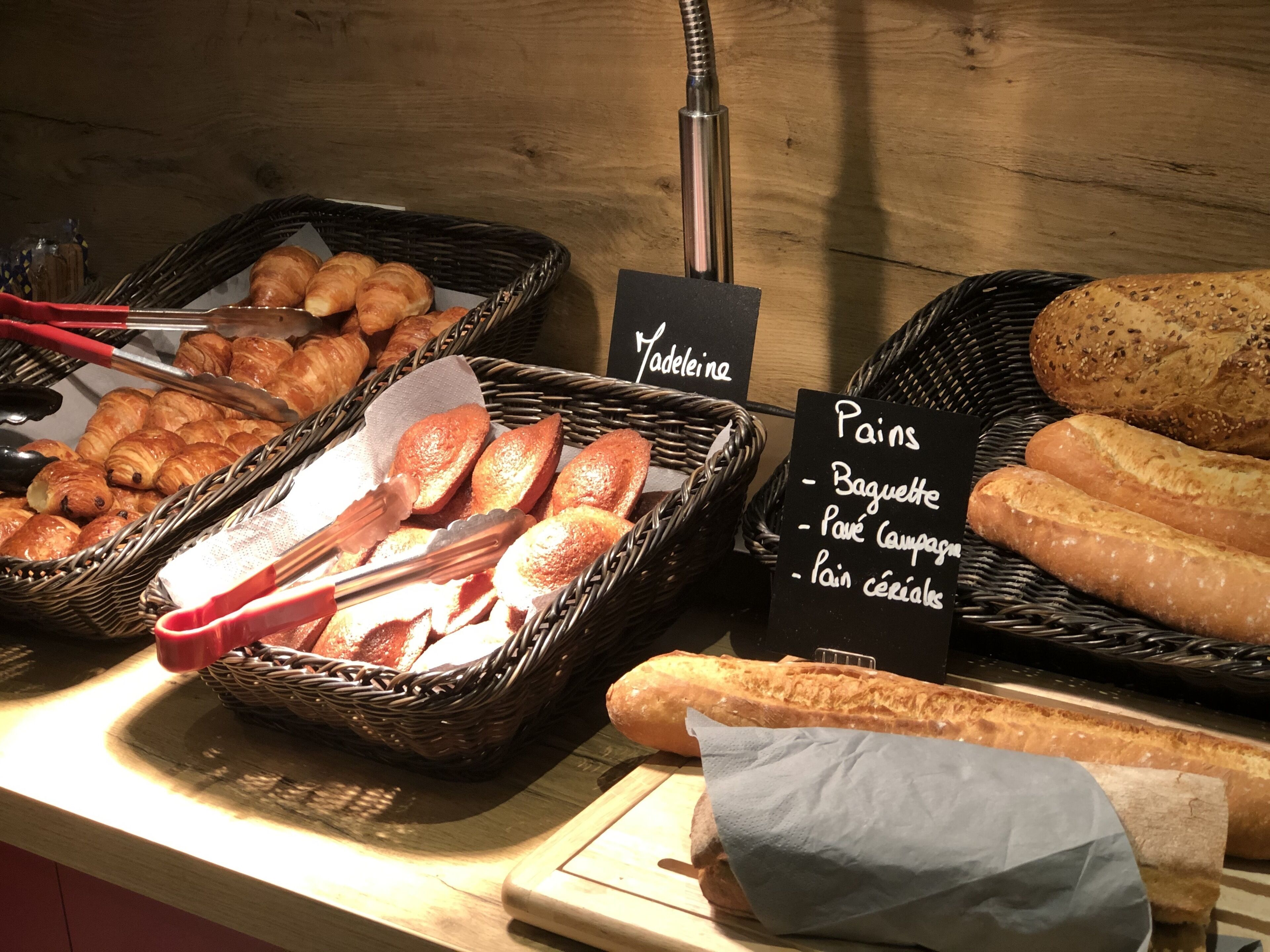 Un expositor de panadería con diversos tipos de pan y pasteles, incluyendo baguettes y croissants, organizados en cestas y sobre una encimera.