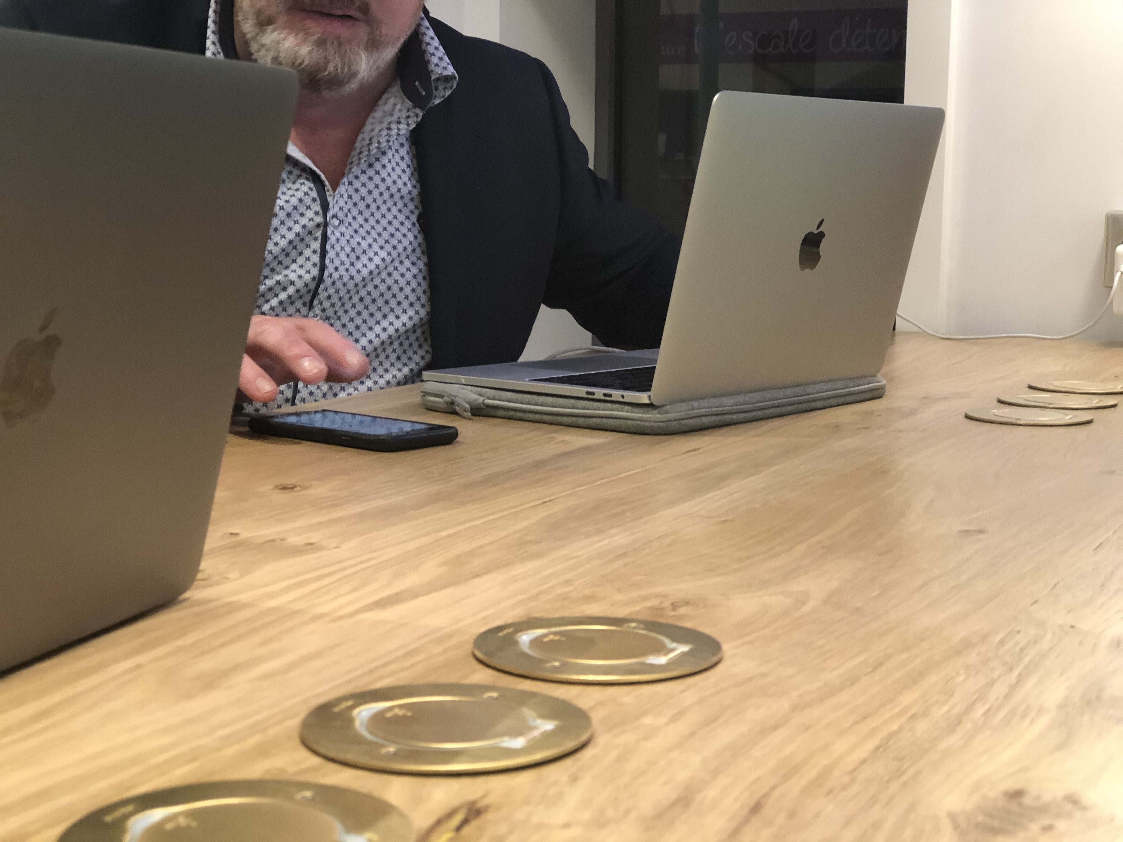 A wooden table with two laptops and a smartphone.