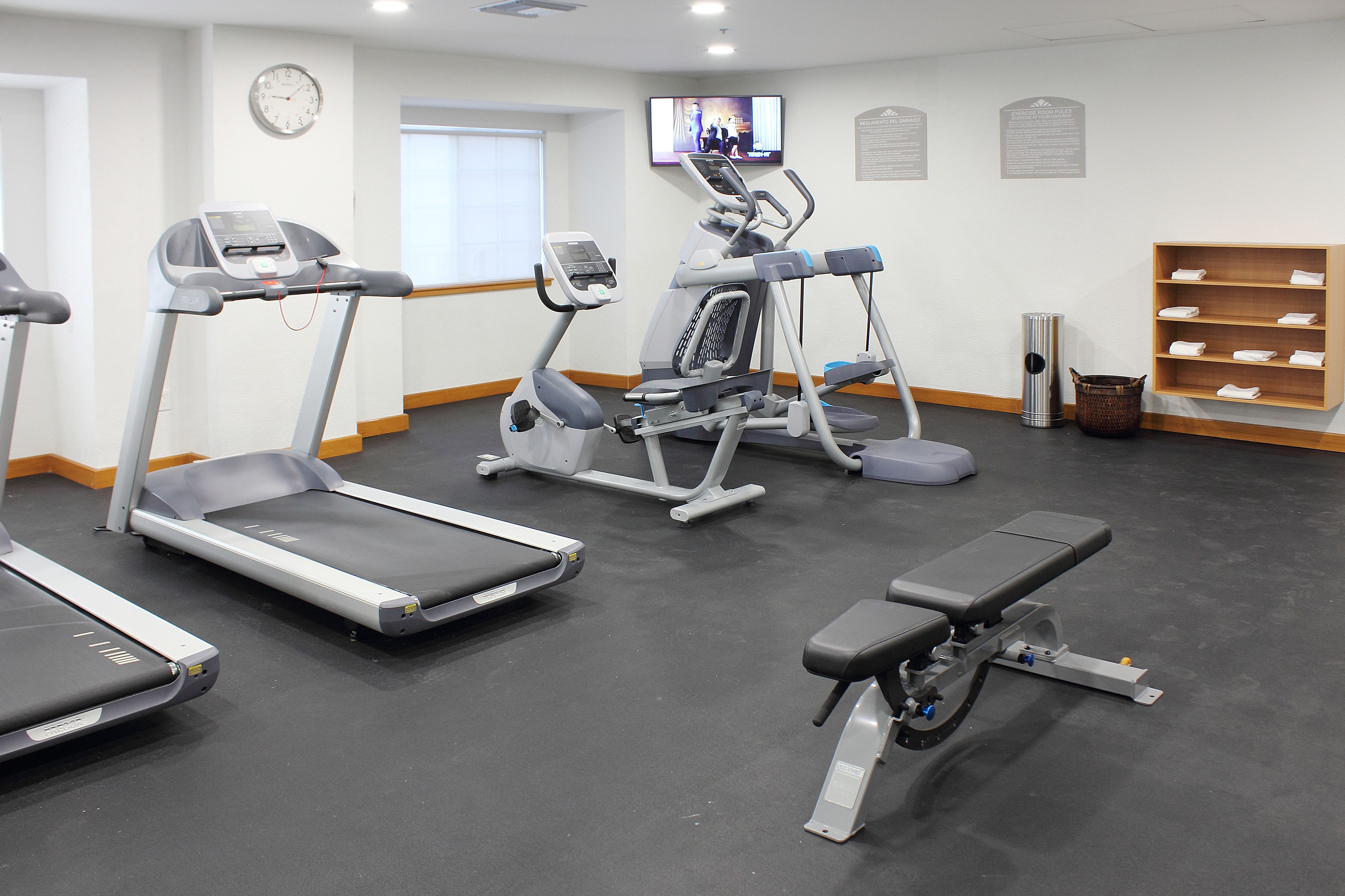 A gym with treadmills, elliptical machines, and a bench.