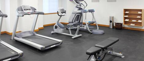 Un gimnasio con cintas de correr, elípticas y una banca.